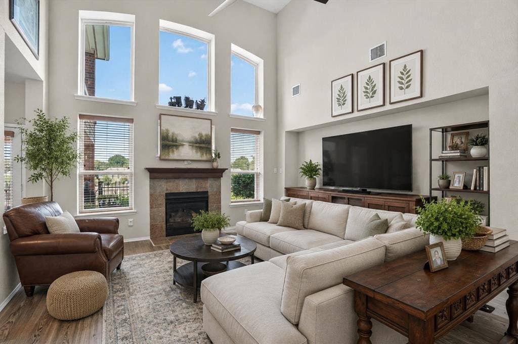 5212 Whisper Drive, Fort Worth, TX 76123 Virtually Staged Two-story living area featuring a tile-surround fireplace with wood mantel, a wall of high windows, and wood-finish flooring