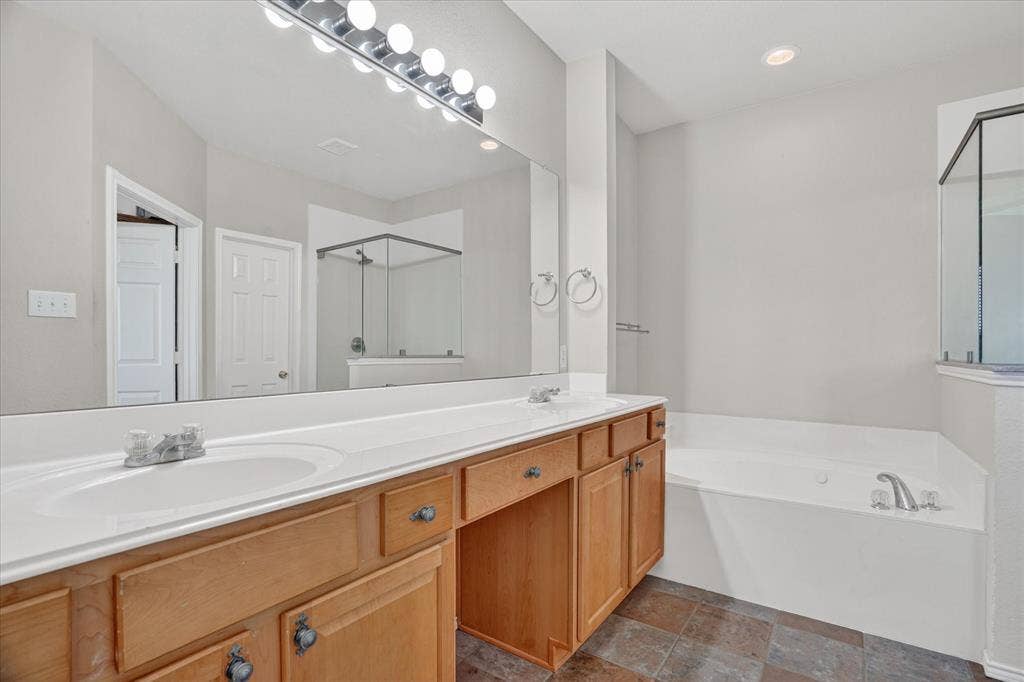 5212 Whisper Drive, Fort Worth, TX 76123 Dual vanity with white undermount sinks and light wood cabinetry, featuring a large wall-mounted mirror and overhead strip lighting