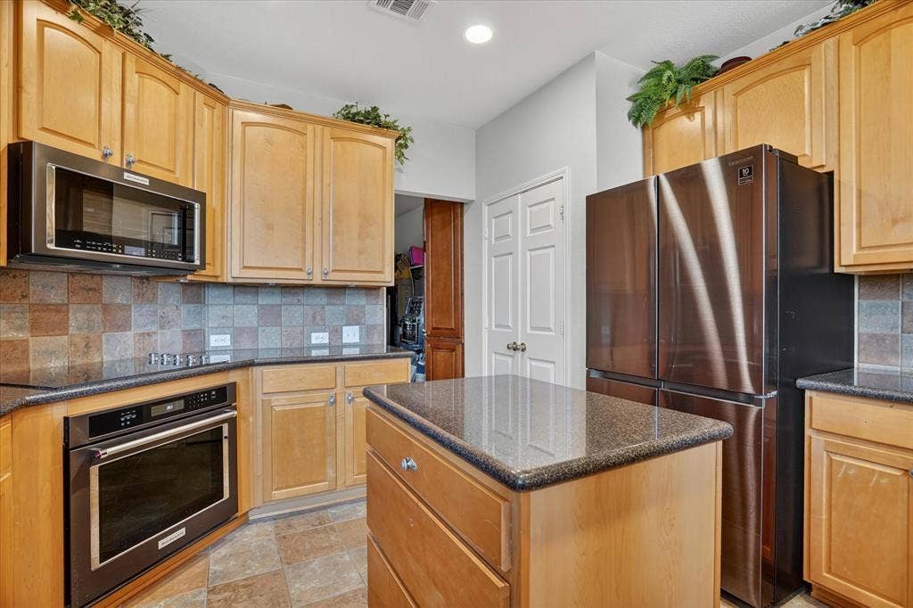 5212 Whisper Drive, Fort Worth, TX 76123 Kitchen featuring light wood cabinetry, dark countertops, built-in microwave, and stainless steel refrigerator