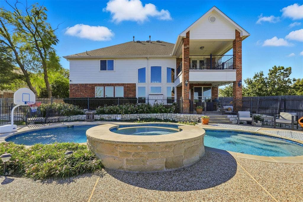 5212 Whisper Drive, Fort Worth, TX 76123 Back of house with a balcony, a patio, brick siding, and a pool with connected hot tub