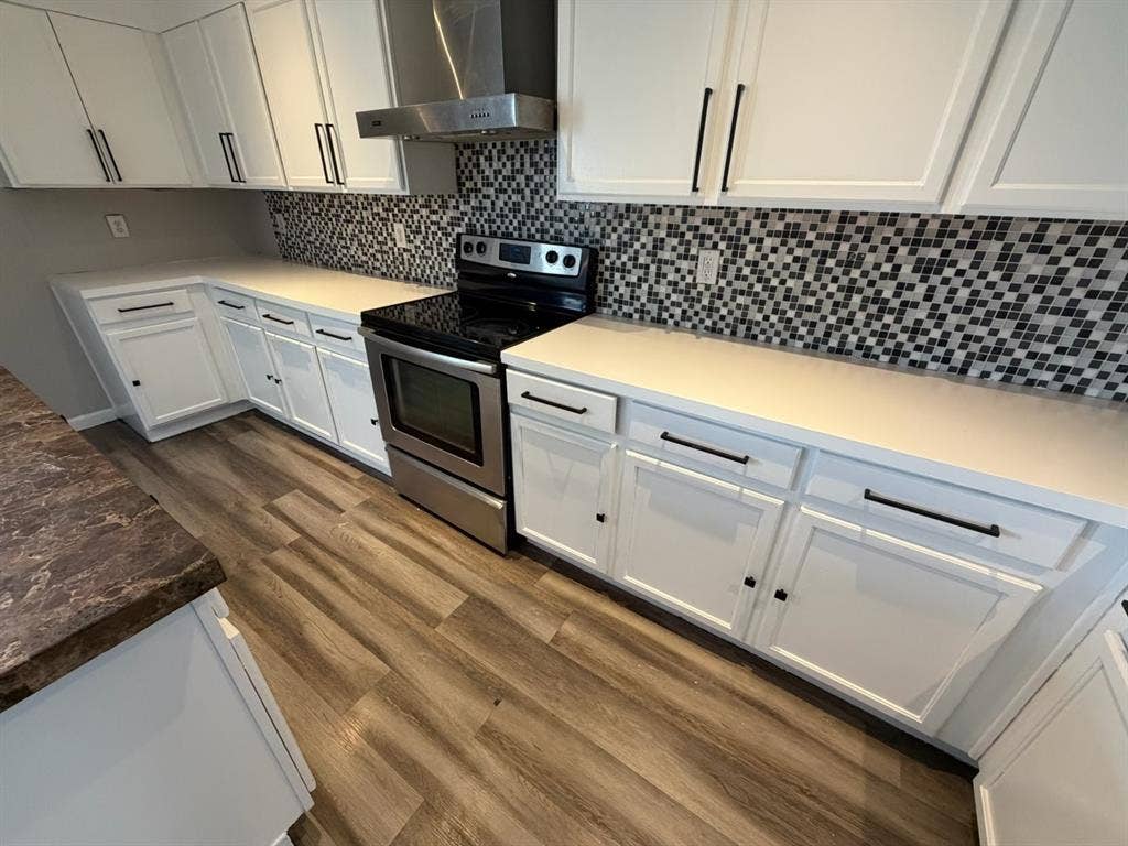 Modern kitchen featuring white cabinetry with black hardware, white countertops, a mosaic tile backsplash, wood-finish flooring, and stainless steel appliances