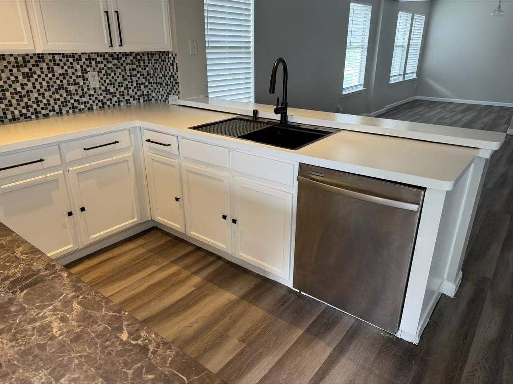 Modern kitchen featuring white cabinetry, a black square sink with a gooseneck faucet, light-toned countertops, a mosaic tile backsplash, and wood-finish flooring