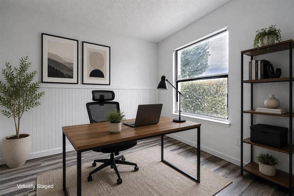 Light-filled interior space featuring white walls with wainscoting, wood-finish flooring, and a large window