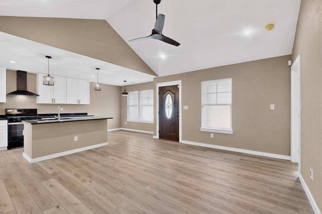 Kitchen with dark countertops, open floor plan, a center island with sink, gas stove, and pendant lighting