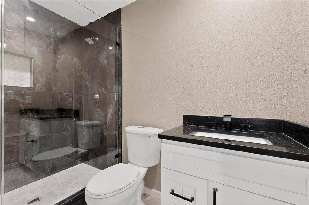 Bathroom with vanity, a textured wall, and a stall shower