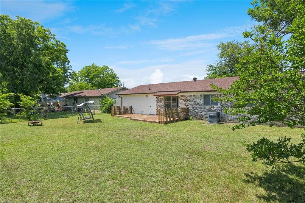 5820 Shipp Drive, Watauga, TX 76148 Expansive green lawn with a brown wood-finish deck and a stone exterior