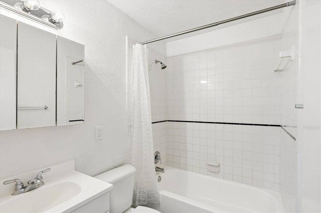 5820 Shipp Drive, Watauga, TX 76148 Bathroom featuring a white vanity with integrated sink, chrome faucet, wall-mounted mirrored medicine cabinet, and a shower-over-tub combination with white subway tile surround and a black accent border