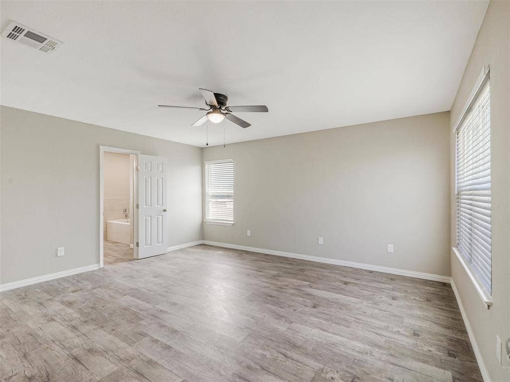 Spacious bedroom featuring wood-finish flooring, a ceiling fan with integrated lighting, and a window with blinds
