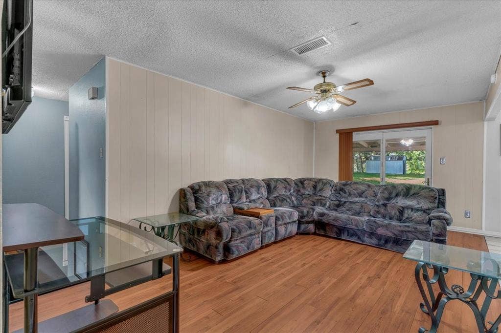 905 SE 3rd Street, Grand Prairie, TX 75051 Living area with hardwood / wood-style floors, a textured ceiling, a ceiling fan, and wooden walls