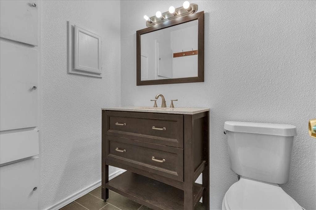905 SE 3rd Street, Grand Prairie, TX 75051 Half bathroom featuring a textured wall, vanity, and dark tile patterned floors
