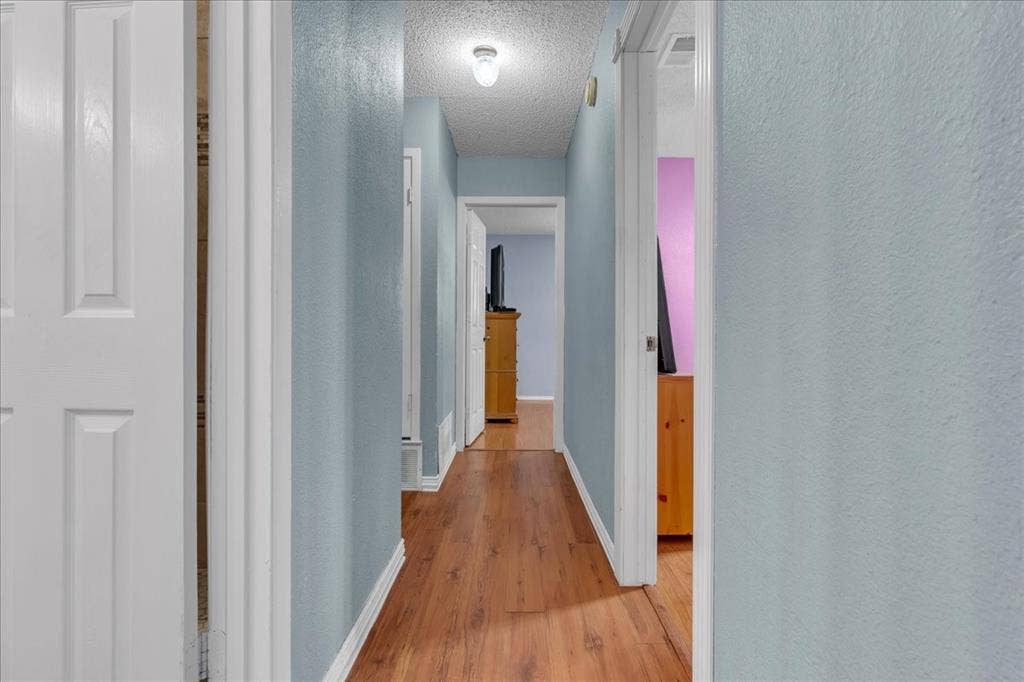 905 SE 3rd Street, Grand Prairie, TX 75051 Hallway with light wood-type flooring, a textured ceiling, and a textured wall
