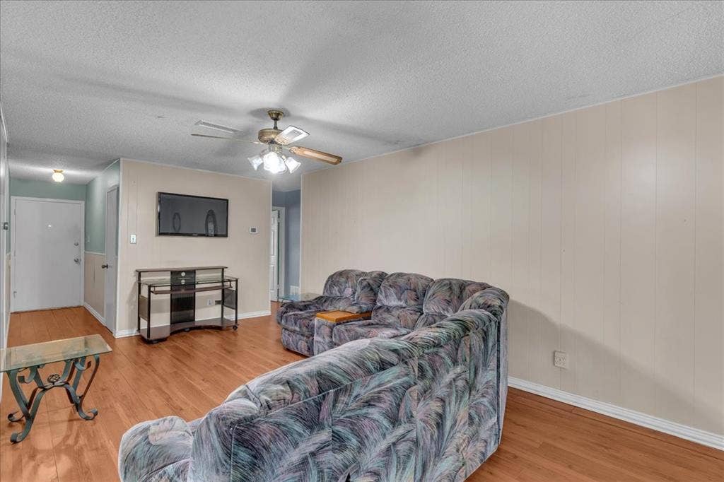 905 SE 3rd Street, Grand Prairie, TX 75051 Living area with a ceiling fan, light wood-style floors, a textured ceiling, and wood walls