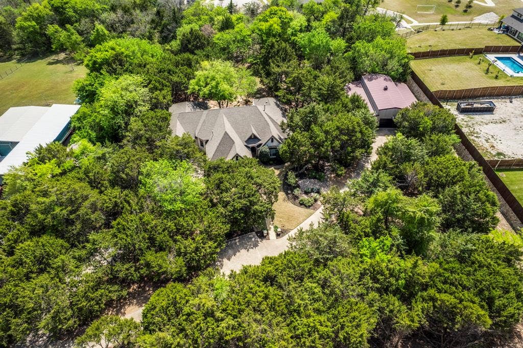 Aerial view of property featuring home, detached workshop, and tree lined setting with driveway.