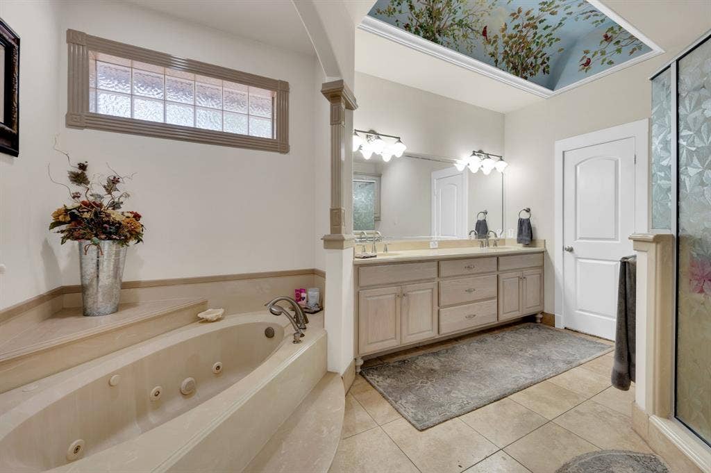 Primary bathroom with jetted soaking tub, dual vanities, and decorative ceiling detail.