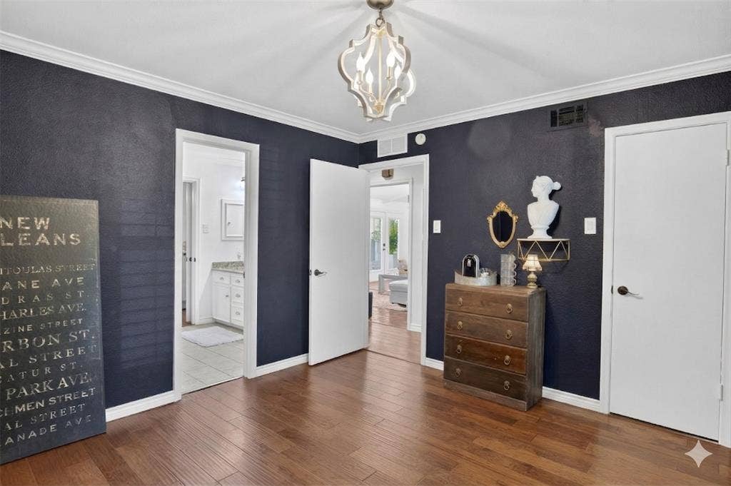 Bedroom featuring ornamental molding, dark wood-style floors, connected bathroom, and suspended lighting