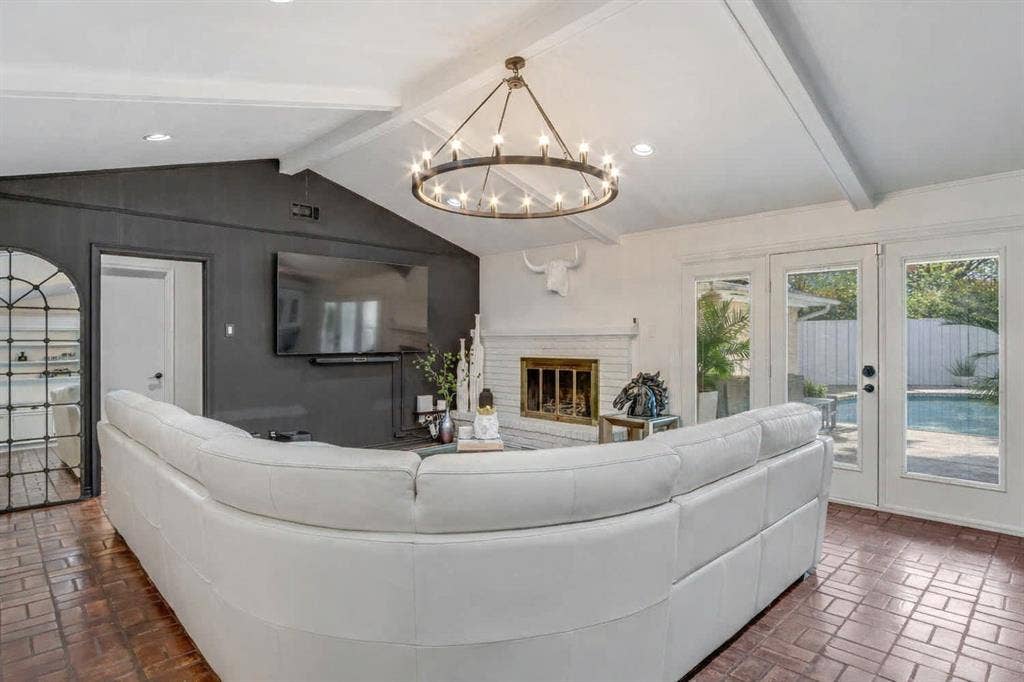 Living room featuring brick flooring, beamed ceiling, french doors, a brick fireplace, and a chandelier
