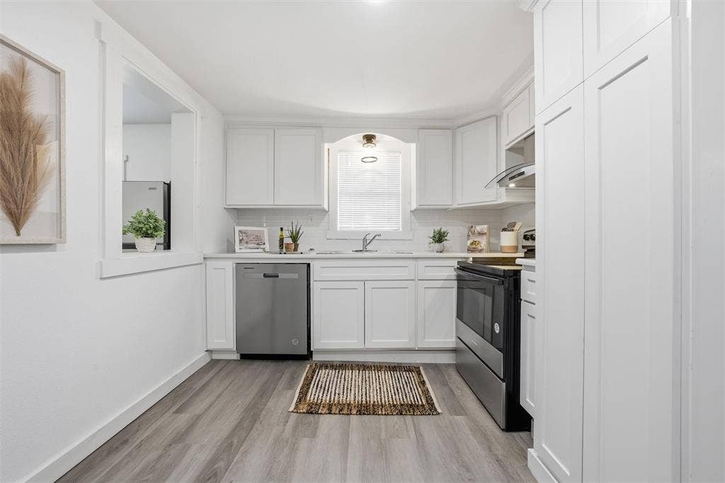 1116 Houston Street, Waco, TX 76704 Kitchen featuring white cabinets, light countertops, stainless steel appliances, light wood-style flooring, and tasteful backsplash
