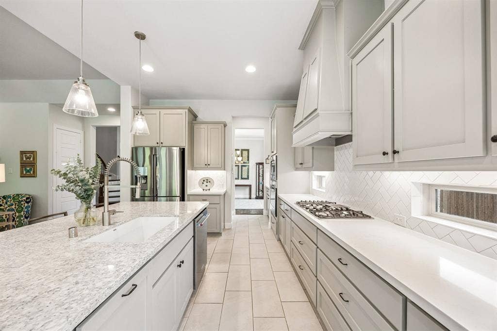 Thoughtfully designed chef's kitchen with a long, linear footprint that maximizes  counter space and storage. The heart of this kitchen features an over-sized central island with quartz countertops, a large undermount sink and pull-out trash drawer. Shaker-style cabinetry perfectly complimenting the integrated  stainless appliances and drop in gas cooktop. Large walk-in pantry between the kitchen and formal dining room seen in the background.