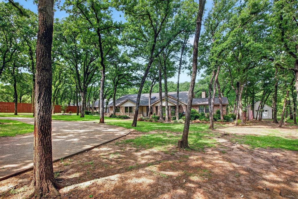 1607 N Main Street, Euless, TX 76039 The property features an extensive yard with mature trees, a well-maintained lawn, and a paved driveway leading to the residence