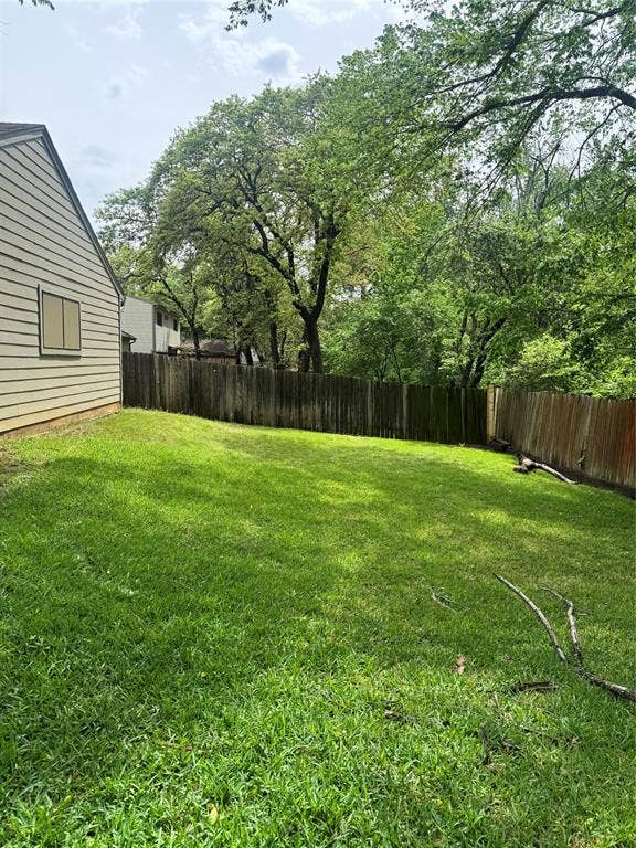 2301 Holly Drive, Euless, TX 76039 Expansive grassy backyard featuring a wood fence, mature trees providing natural shading, and horizontal siding on the property exterior