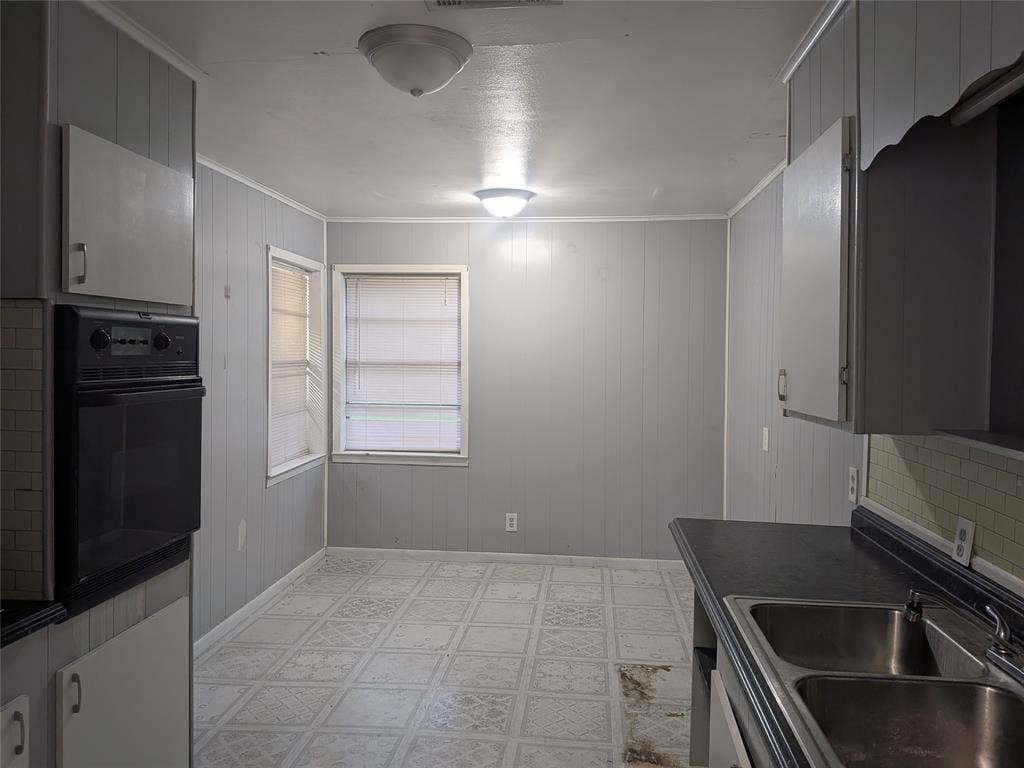 2009 County Road 4619, Athens, TX 75752 Kitchen featuring light flooring, dark countertops, black oven, wooden walls, and gray cabinetry
