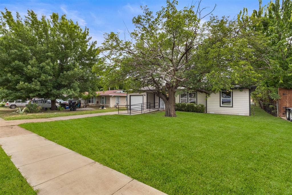 425 Browning Drive, Arlington, TX 76010 Front exterior showcasing a broad lawn, mature trees, a concrete sidewalk, a ramp entry, and vinyl siding