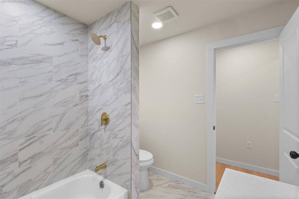 425 Browning Drive, Arlington, TX 76010 Bathroom featuring a white bathtub, gold-finish shower fixtures, and marble-look wall and floor tiling