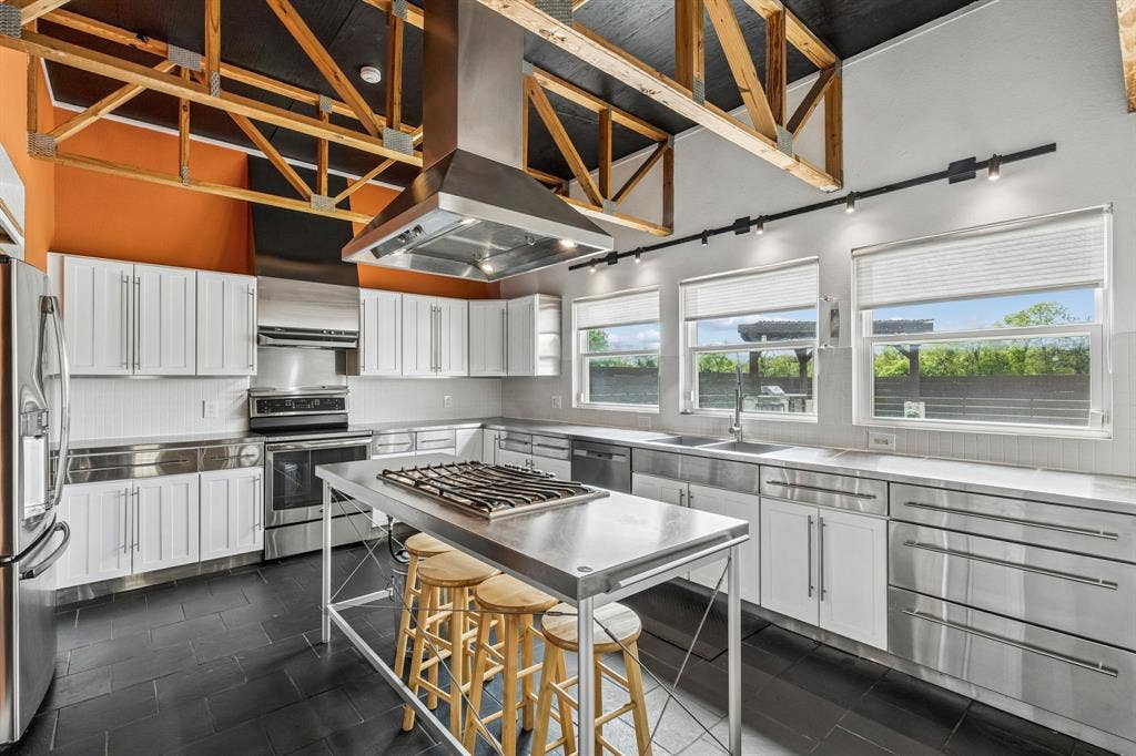6360 Curtis Street, Plano, TX 75093 Custom kitchen with electric oven, dishwasher, refrigerator and tile flooring. The island is mobile and there is a gas tank underneath for the center grill. Professionally installed commercial vent a hood above.