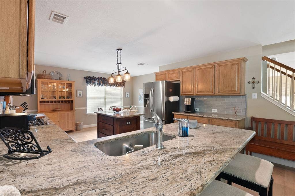 1608 Mountain Laurel Drive, Keller, TX 76248 Kitchen featuring granite countertops, wood-finish cabinetry, stainless steel appliances, a center island with additional storage, and an updated light fixture