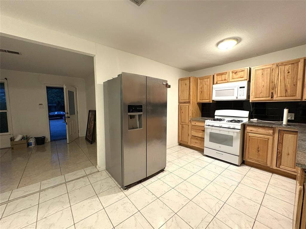 2829 Cecil Drive, Richland Hills, TX 76118 The kitchen features a stainless steel refrigerator, a white gas range with an overhead microwave, wood cabinetry, and tiled flooring