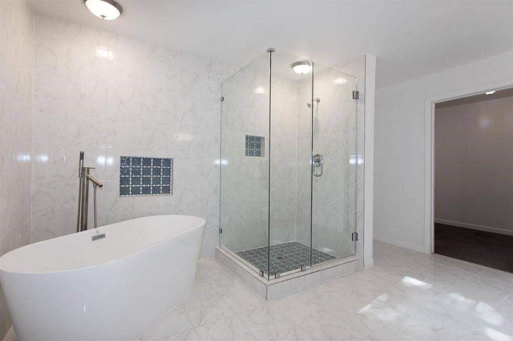 2829 Cecil Drive, Richland Hills, TX 76118 Bathroom featuring a freestanding tub with floor-mounted faucet, a glass-enclosed shower with tiled base, and large format marble-look floor and wall tiles