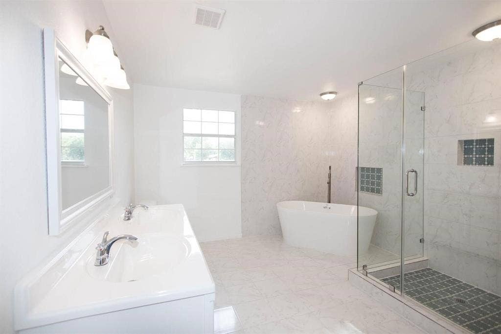 2829 Cecil Drive, Richland Hills, TX 76118 Spacious bathroom featuring a freestanding soaking tub, walk-in shower with clear glass enclosure and tiled floor, dual vanity with undermount sinks, chrome fixtures, and a window providing natural light