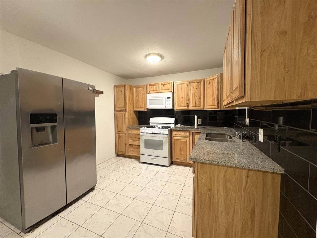 2829 Cecil Drive, Richland Hills, TX 76118 The kitchen features light wood cabinetry, a stainless steel refrigerator, white appliances, and granite countertops