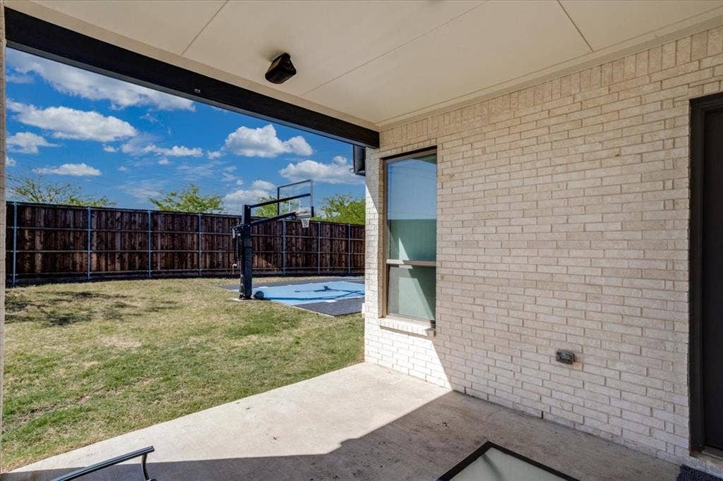Covered patio with built-in speakers overlooks backyard fully equipped with a sports court.