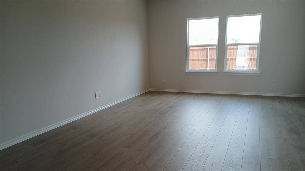 223 Whispering Pine Drive, Royse City, TX 75189 Expansive interior space featuring wood-finish flooring, two large windows, white baseboards, and neutral wall tones