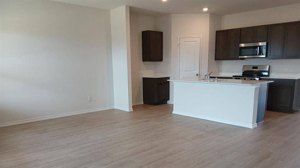 223 Whispering Pine Drive, Royse City, TX 75189 Contemporary kitchen featuring dark wood cabinetry, stainless steel appliances, a center island with a double basin sink, and wood-finish flooring