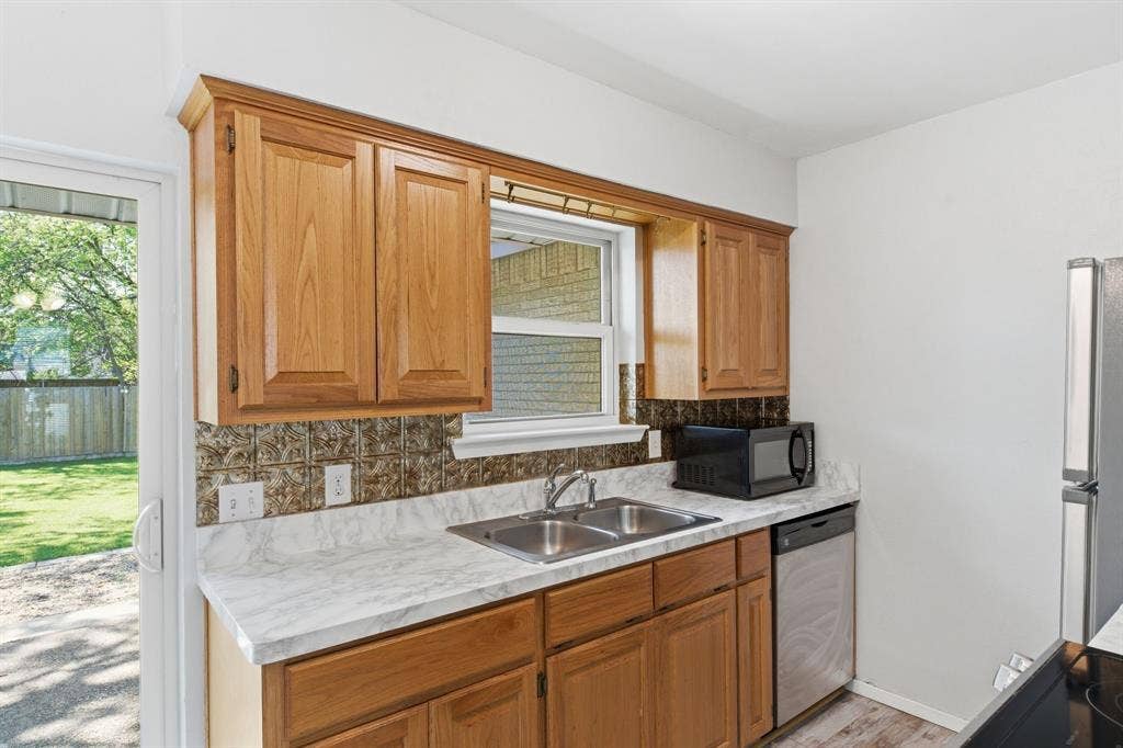 Kitchen featuring light countertops, black appliances, wood finish cabinets, and decorative backsplash