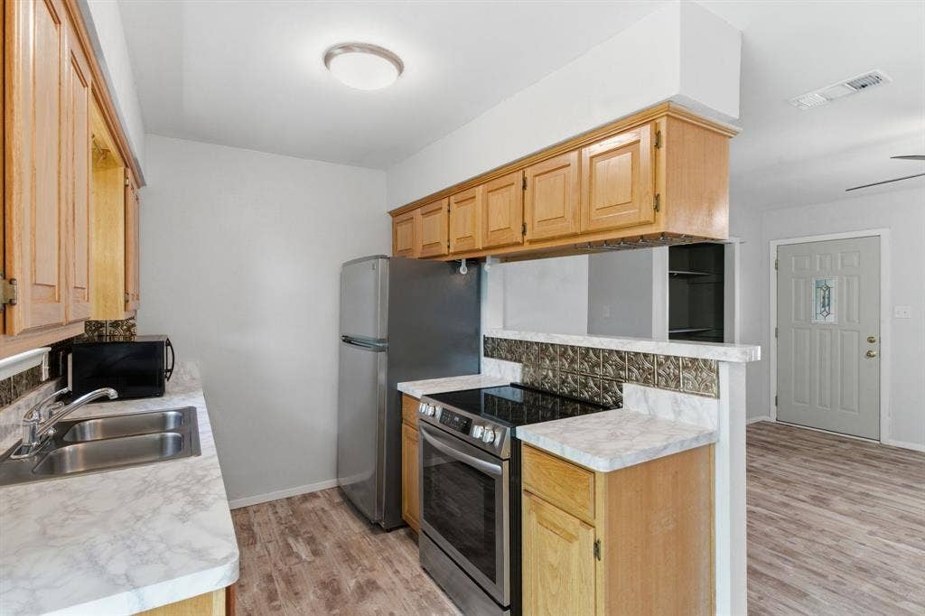 Kitchen with stainless steel appliances, light countertops, light wood-style flooring, tasteful backsplash, and a ceiling fan