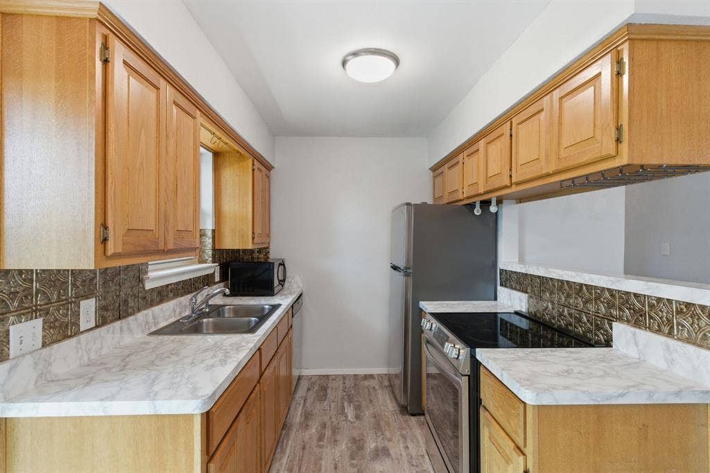 Kitchen featuring backsplash, stainless steel appliances, light countertops, and light wood-style floors