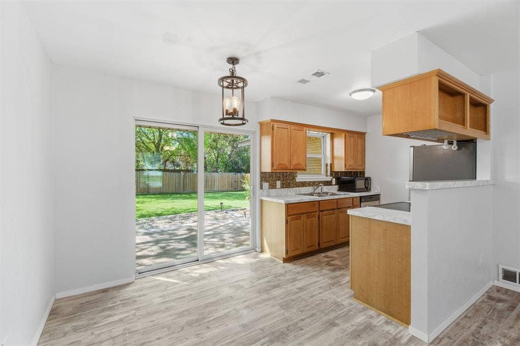 Kitchen featuring light countertops, light wood finished floors, open shelves, black microwave, and backsplash
