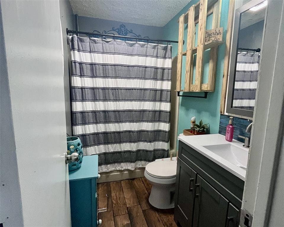 3020 Delaware Trail, Lake Worth, TX 76135 Bathroom with a textured ceiling, a shower with shower curtain, wood finished floors, toilet, and vanity