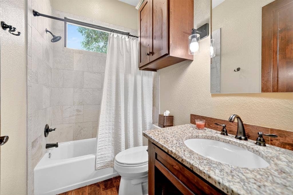 15491 Presidio Circle, Caney City, TX 75148 Bathroom featuring a granite-finish countertop vanity with an undermount sink, dark wood-finish cabinetry, and a shower/tub combination with light-toned tile surround and dark bronze fixtures