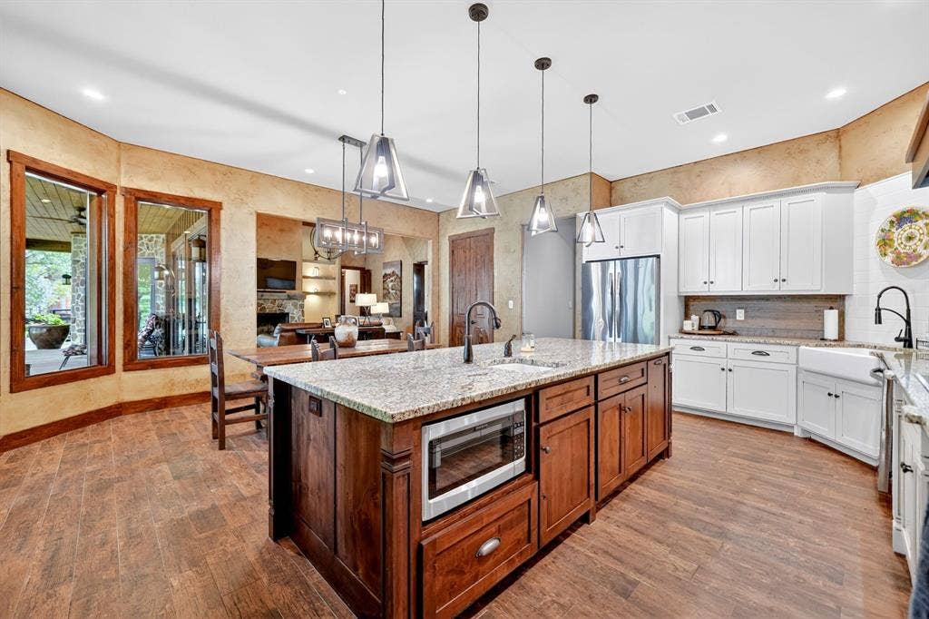 15491 Presidio Circle, Caney City, TX 75148 Spacious kitchen featuring a large central island with granite countertop, wood-finish flooring, white upper and lower cabinetry, and a farmhouse-style sink