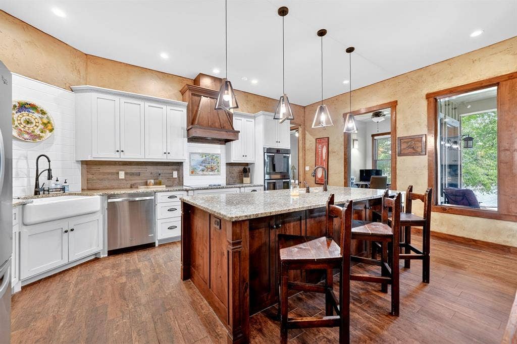 15491 Presidio Circle, Caney City, TX 75148 Living area featuring a stone fireplace with built-in shelving, exposed wood ceiling beams, wood-finish flooring, a wood-paneled exterior door, and a craftsman-style entry door
