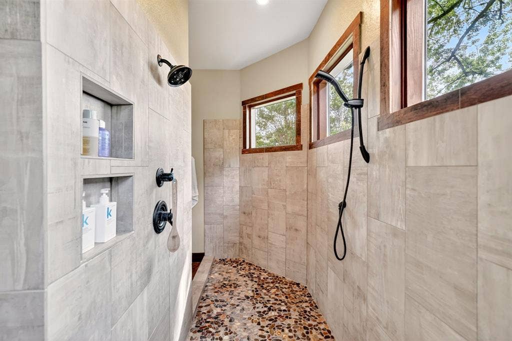15491 Presidio Circle, Caney City, TX 75148 Shower featuring light-toned large format tile walls, dual recessed shower niches, dark bronze shower fixtures, and a pebble tile floor