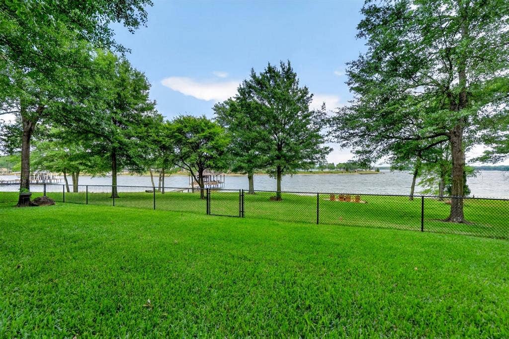15491 Presidio Circle, Caney City, TX 75148 Expansive lawn area with a black chain-link fence and gate, bordered by mature trees