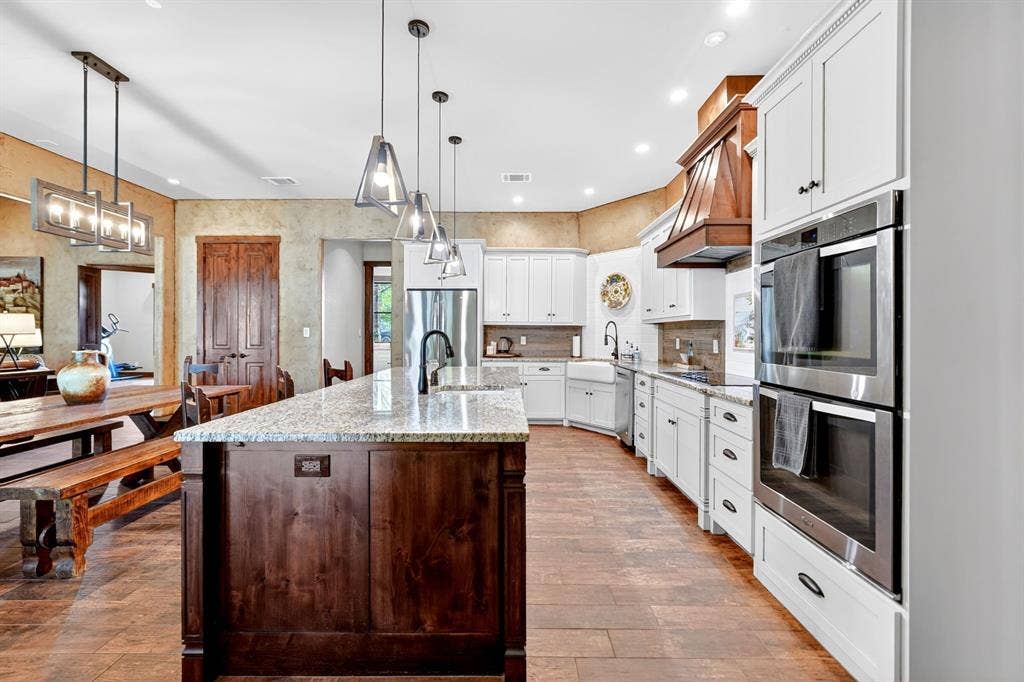 15491 Presidio Circle, Caney City, TX 75148 Gourmet kitchen featuring a substantial island with stone countertops, a farmhouse-style sink, white shaker cabinetry, stainless steel double ovens, and wood-finish flooring