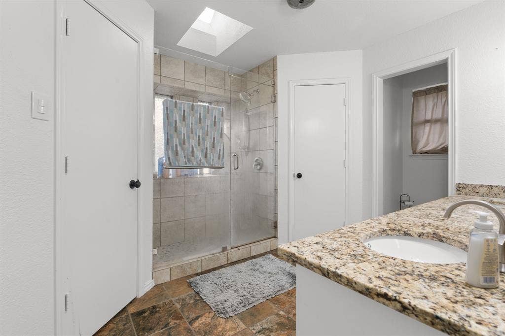 4200 Jennifer Lane, Crowley, TX 76036 Full bathroom featuring double vanity, a shower stall, stone tile floors, and a skylight