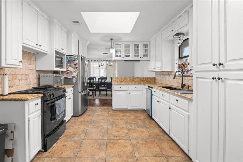 4200 Jennifer Lane, Crowley, TX 76036 Kitchen featuring a skylight, white cabinets, stainless steel appliances, a peninsula, and light stone countertops