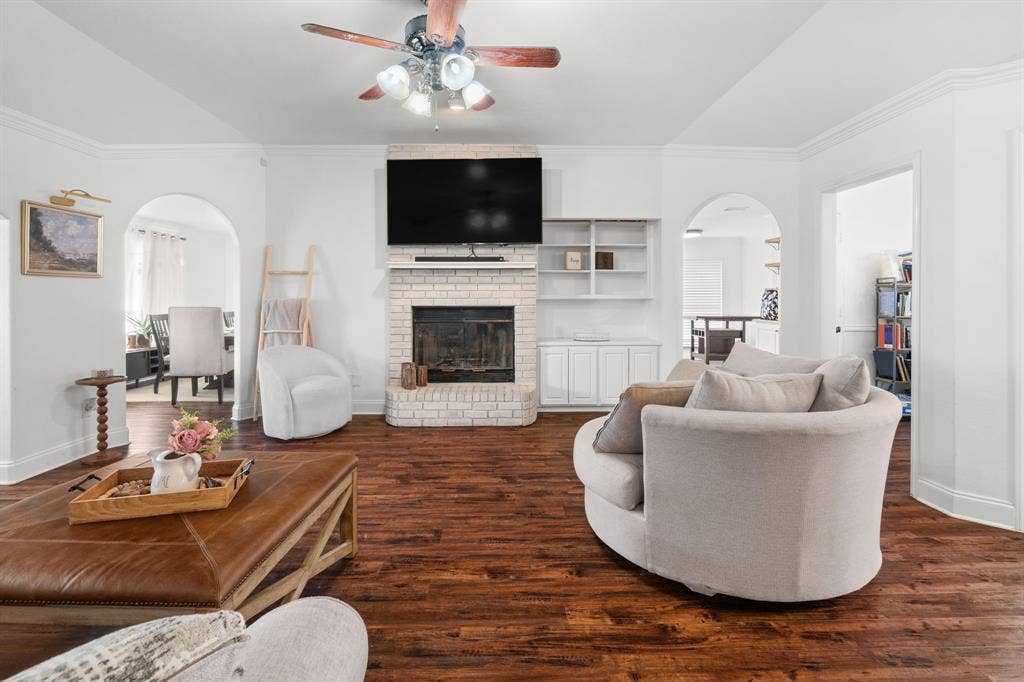 4200 Jennifer Lane, Crowley, TX 76036 Living room featuring arched walkways, crown molding, dark wood-style floors, ceiling fan, and a brick fireplace
